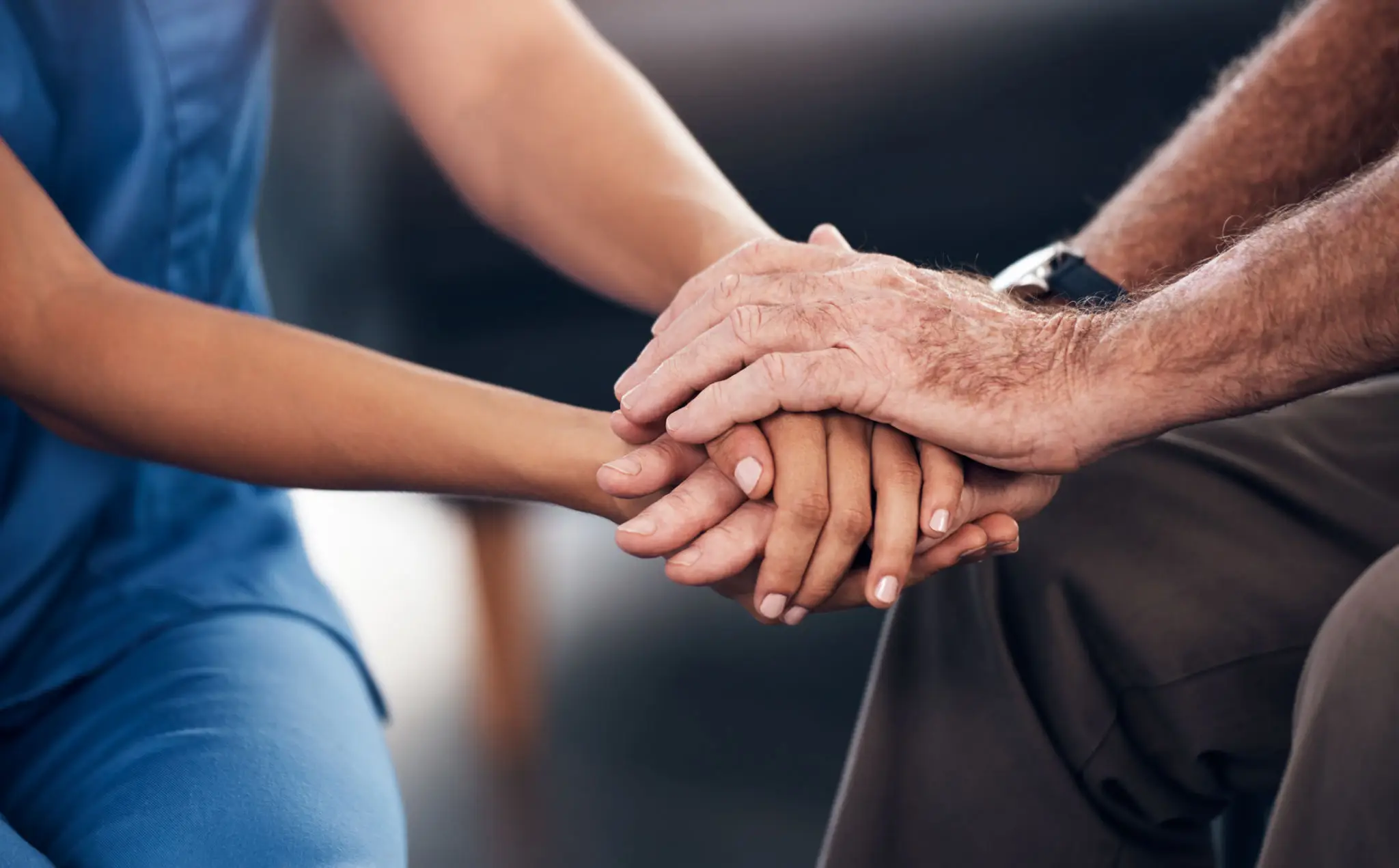 Elderly and caregiver hands clasped together